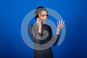 Image of a happy surprised shocked young pretty woman posing isolated over blue background using mobile phone