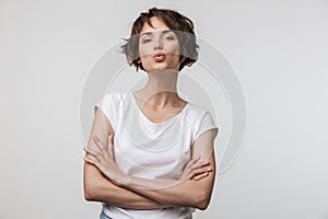 Image of happy woman in basic t-shirt looking at camera while standing with arms crossed