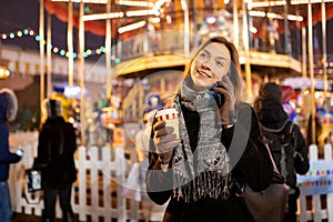Image of happy woman with glass and phone in hands in evening for walk