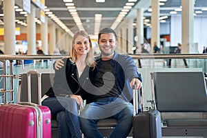 Image of happy woman and man in love looking at camera while sitting in waiting room at airport.