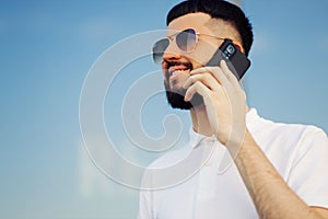 Image of a happy young man walking down the street and looking to the side, talking on a mobile phone