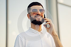 Image of a happy young man walking down the street and looking to the side, talking on a mobile phone