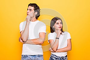 Image of happy young people man and woman in basic clothing thinking and touching chin while looking aside over yellow background