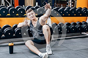 Image of happy young sportsman sitting in gym and make selfie.