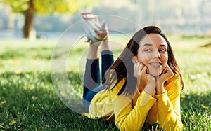 Image of happy young teenage girl smiling and relaxing outside in nature green park. Cheerful young beautiful woman lying outdoors