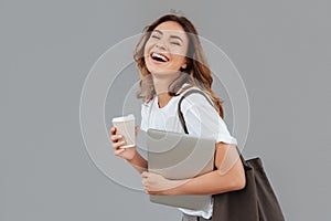 Image of happy young woman 20s laughing and standing over gray w