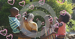 Image of hearts over happy african american family making soap bubbles in garden