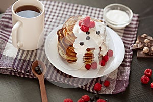 Image of home made pancakes with sour cream on white plate decorated with berries, fresh blueberries and raspberries, cup of tea