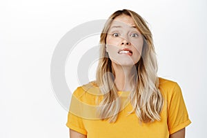Image of hopeful cute blond girl yearning, want, look with desire and hope, stands in yellow t-shirt over white