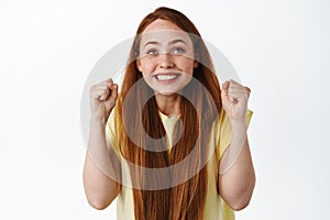 Image of hopeful girl looking up at screen with clenched fists and excited smiling face, rooting for team, cheering and