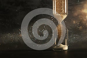 Image of hourglass as time passing concept over black background for business deadline. Glitter overlay.