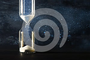 Image of hourglass as time passing concept over black background for business deadline. Glitter overlay.