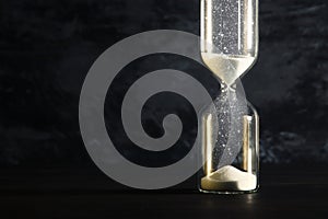 Image of hourglass as time passing concept over black background for business deadline. Glitter overlay.