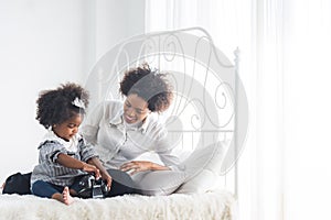 Image of joyful african american woman and her little daughter sleeping together in bed at home