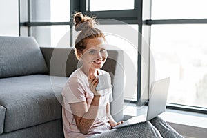 Image of joyful redhead woman drinking coffee and using laptop