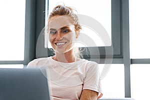 Image of joyful redhead woman smiling and using laptop