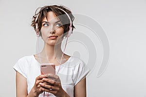 Image of joyful woman in basic t-shirt holding smartphone while listening to music with headphones