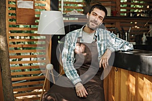 Image of joyous waiter boy sitting at the bar while working in cafe or coffeehouse outdoor