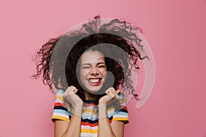 Image of joyous woman 20s with curly hair rejoicing and smiling, isolated over pink background