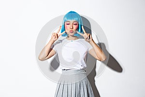 Image of kawaii asian woman in blue shirt wig, shows peace gesture and pout. Girl in halloween costume enjoys party