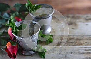 Image for Kentucky Derby in May showing two silver mint julep cups with crushed ice and fresh mint in a rustic setting.