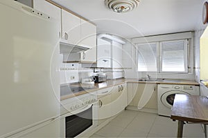 Image of a kitchen with white wood cabinets with cherry accents, built-in white appliances, white aluminum window, and wood