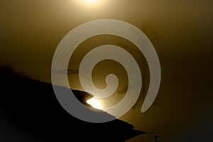 Image of a lake and a tree with the sunrise in backlight