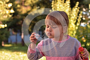 Image of little girl blowing air bubble balloons with view of green trees and park in the background