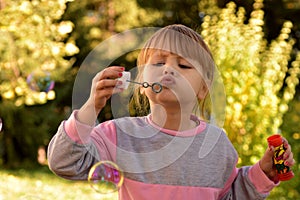 Image of little girl blowing air bubble balloons with view of green trees and park in the background