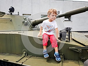 Image of little toddler boy sitting and climbing on tank at military World War museum