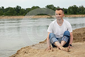 The image lonely positive man sitting on the beach river
