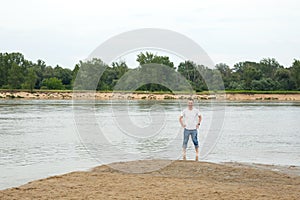 The image lonely positive and smiling man on a beach by the river.