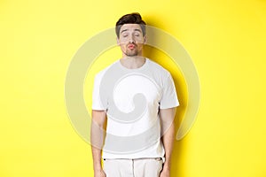 Image of lovely man close eyes and pucker lips, waiting for kiss, standing in white clothes against yellow background
