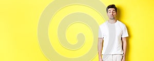 Image of lovely man close eyes and pucker lips, waiting for kiss, standing in white clothes against yellow background