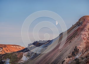 lunar landscape of Icelandic mountains with the moon in the blue sky