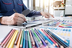 Image of male creative graphic designer working on color selection and drawing on graphics tablet at workplace with work tools