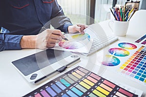 Image of male creative graphic designer working on color selection and drawing on graphics tablet at workplace with work tools