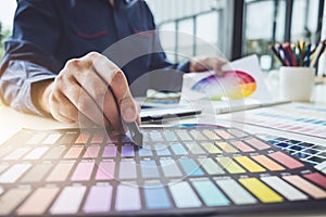 Image of male creative graphic designer working on color selection and drawing on graphics tablet at workplace with work tools
