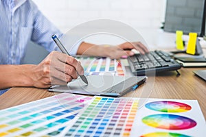 Image of male creative graphic designer working on color selection and drawing on graphics tablet at workplace with work tools and