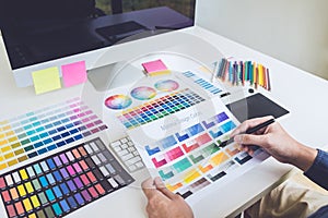 Image of male creative graphic designer working on color selection and drawing on graphics tablet at workplace with work tools and