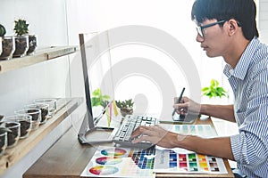 Image of male creative graphic designer working on color selection and drawing on graphics tablet at workplace with work tools and