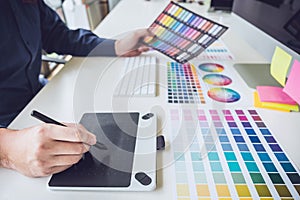 Image of male creative graphic designer working on color selection and drawing on graphics tablet at workplace with work tools and