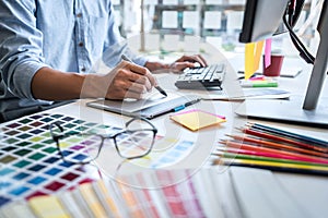 Image of male creative graphic designer working on color selection and drawing on graphics tablet at workplace with work tools and