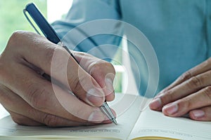 Image of male hand focusing holding a pen to write.  Businessman writing on paper report in office