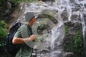 Image of male hiker with backpack enjoying the view of beautiful tropical waterfall