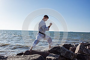 Image of male karate fighter posing on stones sea background