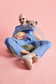 Image of man in 3d-glasses siiting in pajama with popcorn over pastel rose background. photo