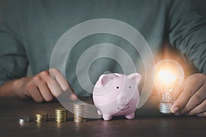 image of man hand holding light bulb with pink piggy bank for account save money.