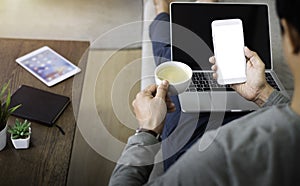 Image of man hand using, holding smartphone or mobile mockup with blank white screen display and laptop computer.