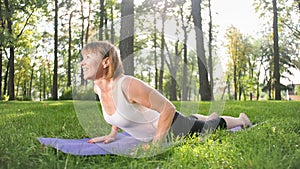 Image of mid aged smiling happy woman meditating and doing yoga exercises on grass at forest. Woman taking care of her